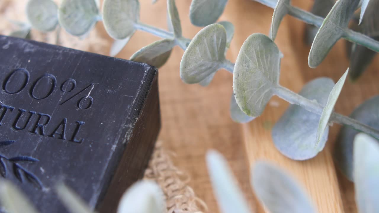 '100% 자연'이라는 단어가 새겨진 검은색 비누 바의 클로즈업, 유칼립투스 잎으로 둘러싸여 있습니다.