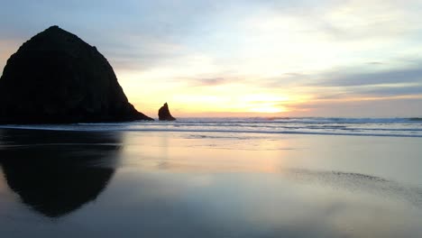 los colores del atardecer se reflejan en la arena en canon beach, oregon.