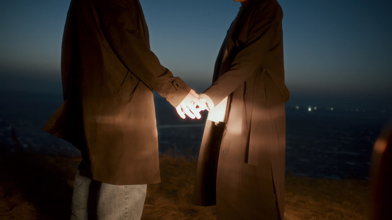 вЂ‹вЂ‹Close-Up of Couple Holding Hands at Night near Dark Frozen Lake