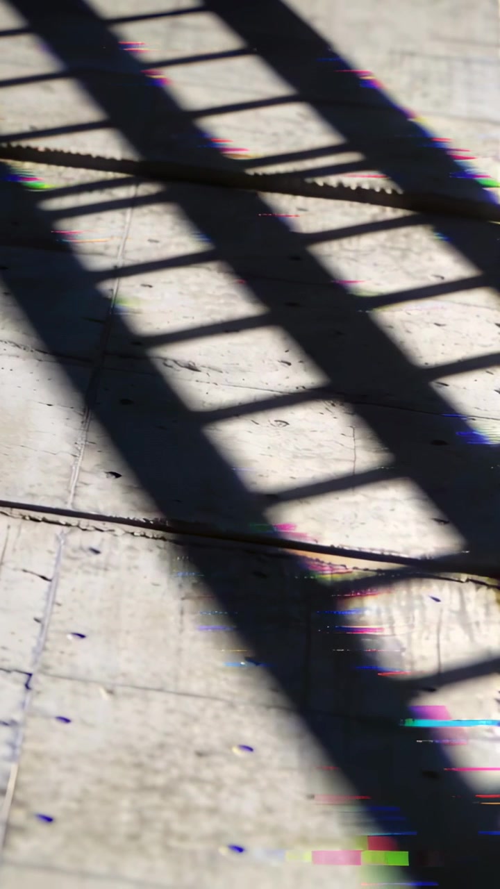 Vertical video: Shifting sun casting grid shadow across pavement moving cable shadow and side bands