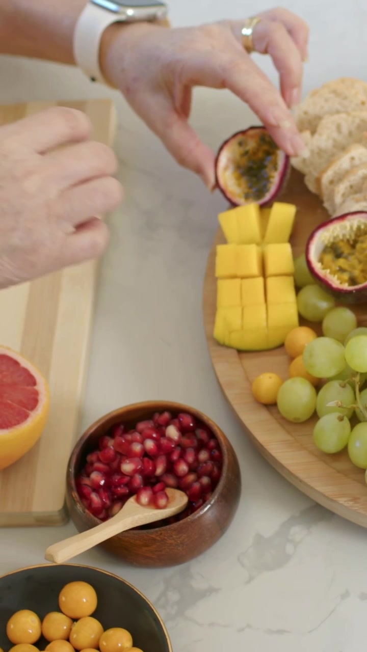 Vídeo vertical: Mãos entrando, anfitrião arrumando bandeja de madeira no balcão, fatiando toranja.
