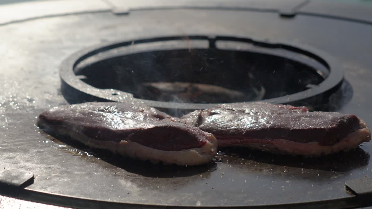 Various seasonings are being sprinkled on top of raw steaks cooking