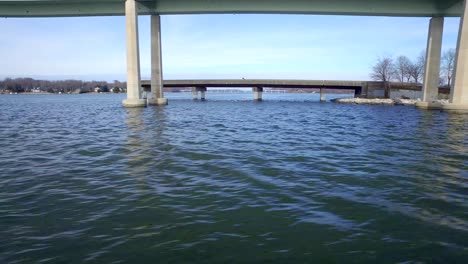 a long aerial shot that starts low on the water with ducks and soars out above a blue river while looking at two bridges carrying car traffic across