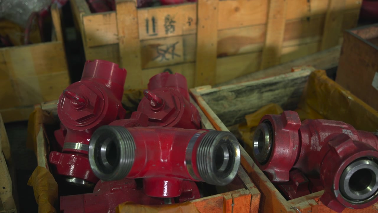 Low-angle close-up shows red-painted metal hose couplings and pipe fittings stacked inside orange-brown wooden crates in workshop storage, with scratched surfaces, threaded openings, and organized