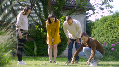 distant view of a caucasian young man calculating distance between petanque balls in the park while his friends looking at him