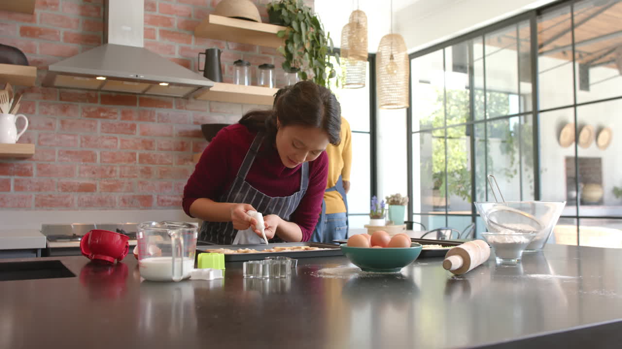 pareja feliz en delantales decorando galletas de navidad en la cocina, espacio de copia, cámara lenta