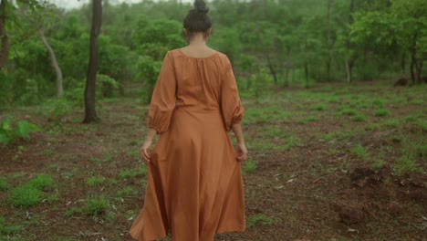 Woman-in-an-orange-dress-walking-in-a-lush-green-forest