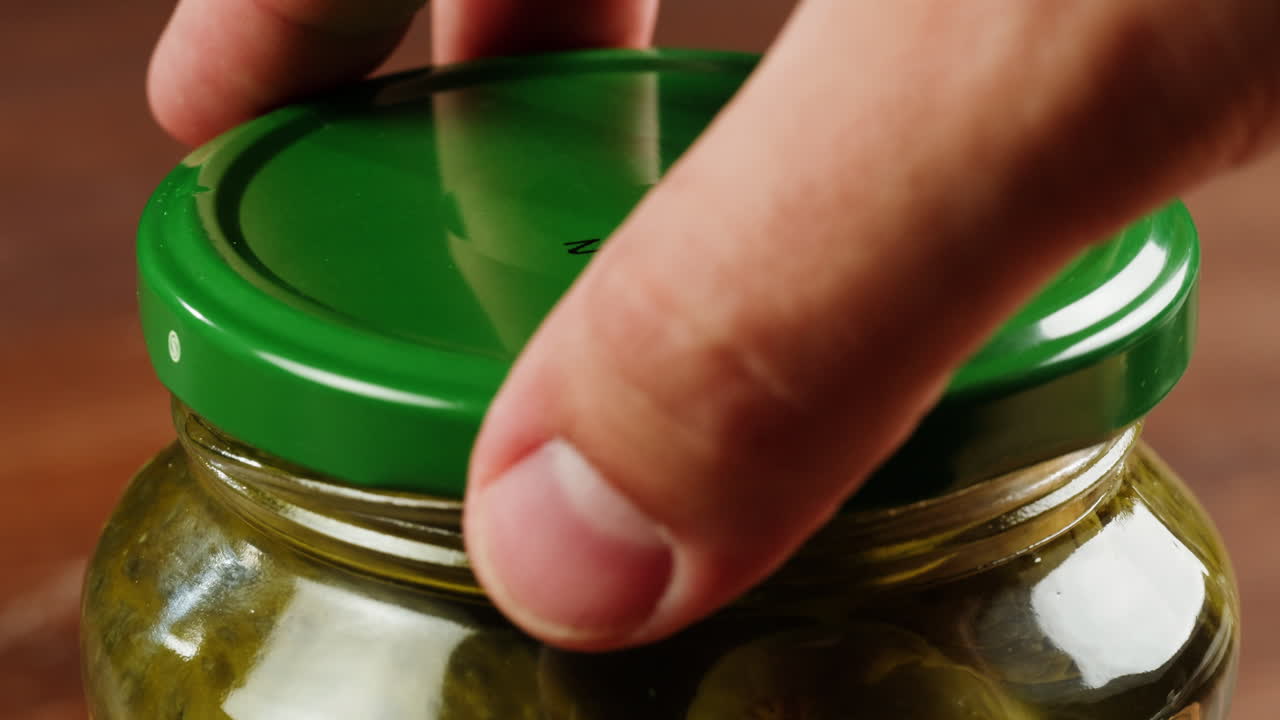 Hand opening a jar of pickles