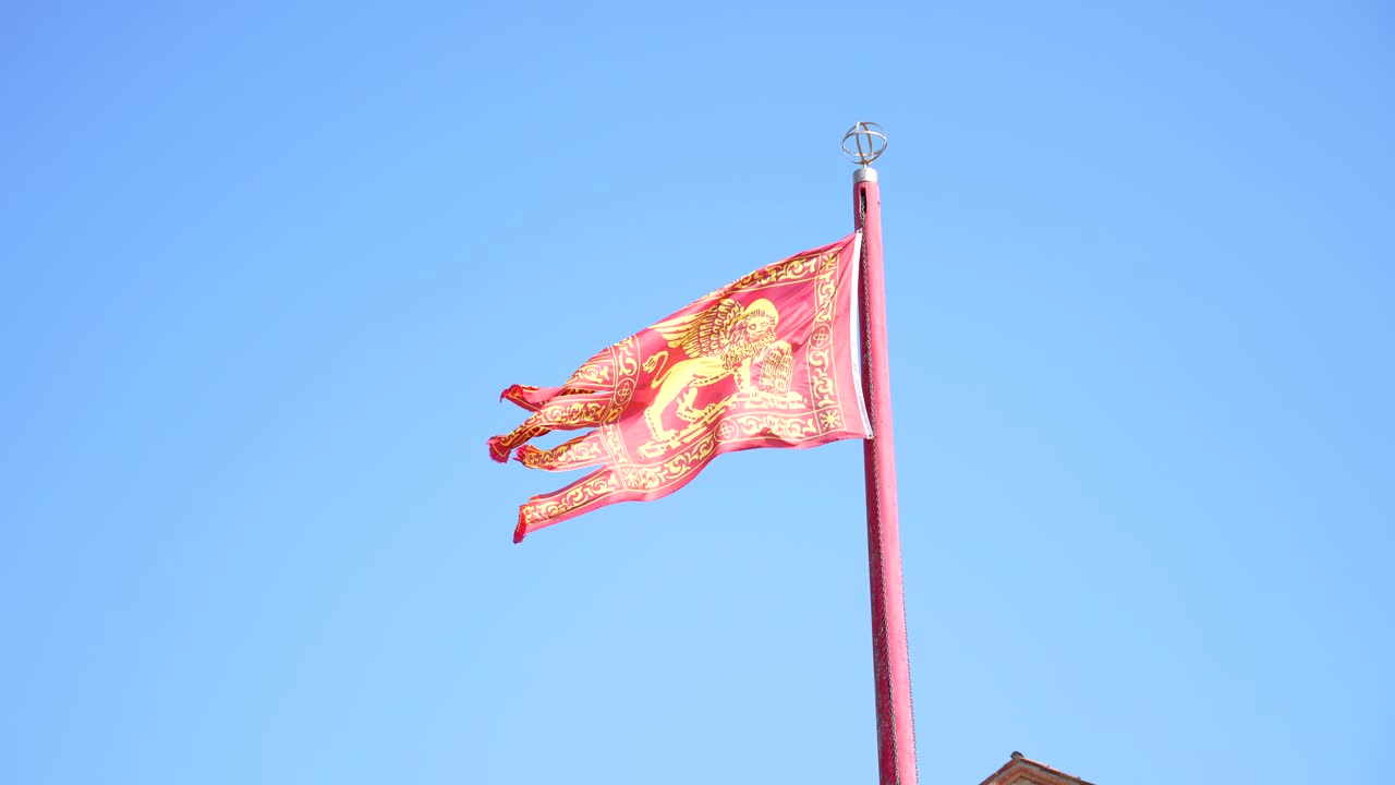 viento fuerte agitando la bandera veneciana roja con un león alado en un día soleado