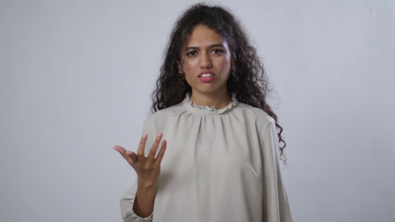 A South Asian woman with curly hair in a beige blouse, showing quiet disapproval or disappointment
