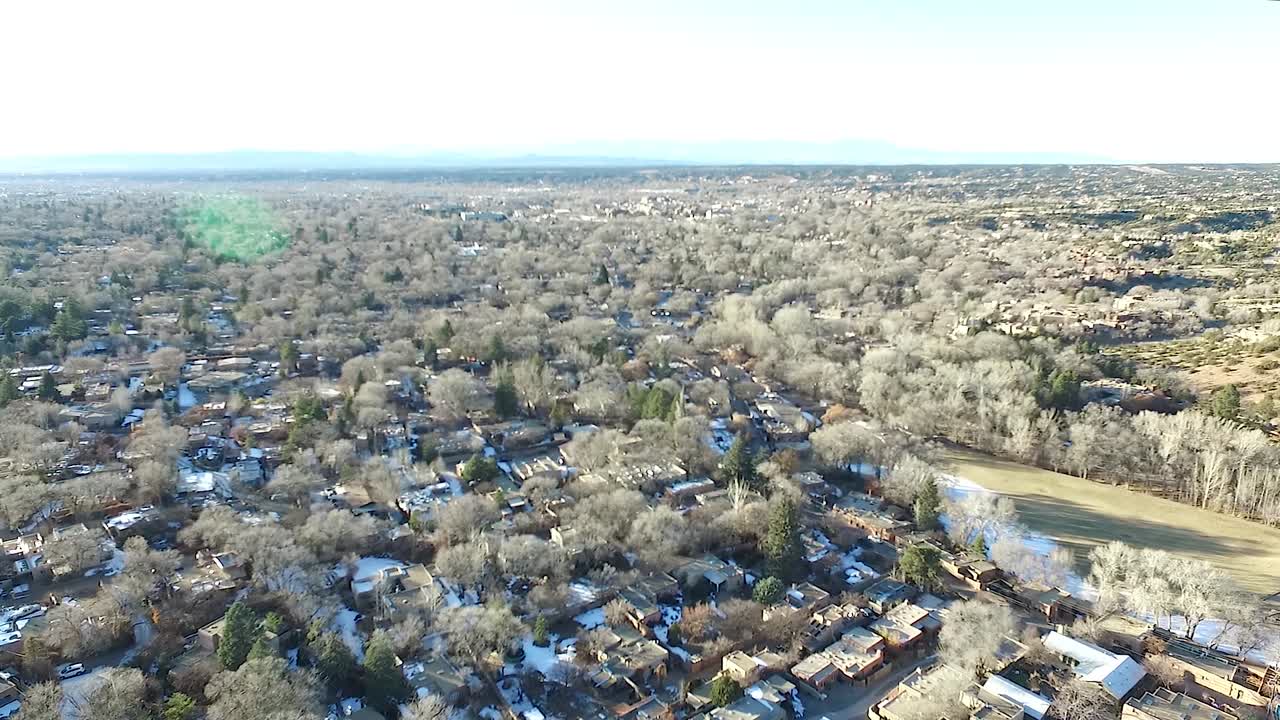 Peaceful aerial footage of Santa Fe, New Mexico in winter, showing patches of snow, warm light flare, and Patrick Smith Park