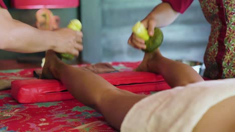 two spa therapists use herbal compresses to massage the tension from the ankles of a patient at an ayurvedic retreat