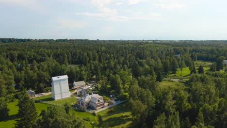 aerial drone footage ascending and flying higher in front of a historic white wooden lighthouse on the sandstone and grassy shoreline of baltic sea during a summer sunny day, forest around it