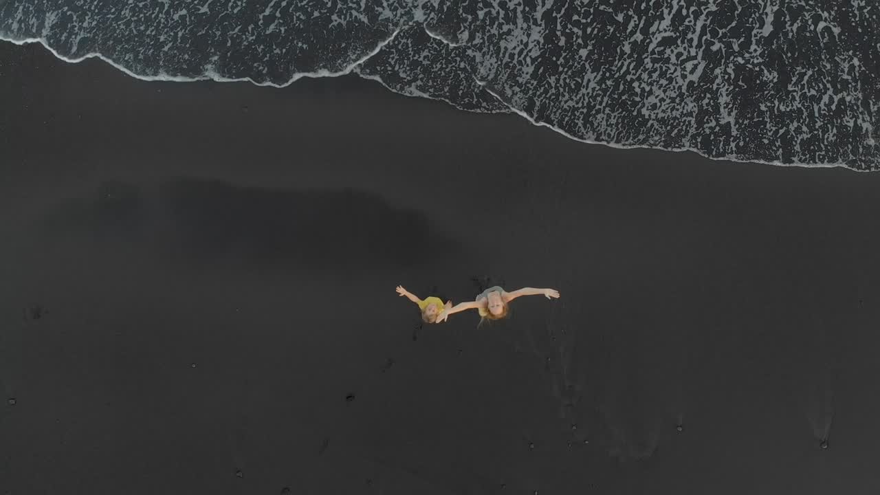 검은 화산 모래 를 가진 해변 에서 산책 하고 재미 를 느끼고 있는 어머니 와 아들 의 공중 촬영