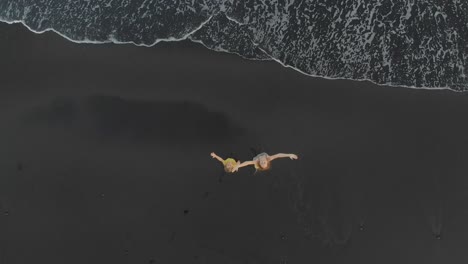 aerial shot of a mother and her son walking and having fun on a beach with a black volcanic sand