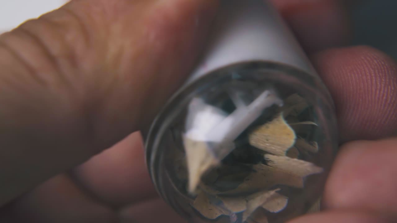 hombre afila un lápiz verde con un afilador en un fondo claro