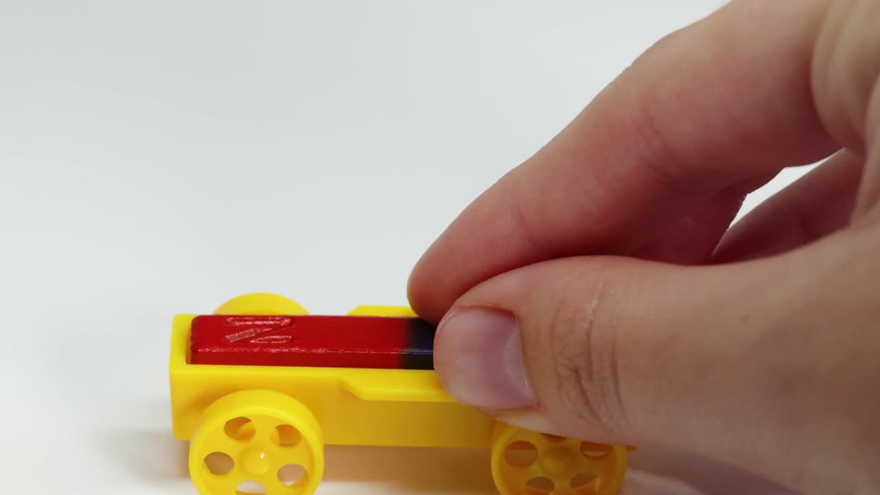 A hand moves yellow magnetic toy cars on a white surface to show magnetic forces