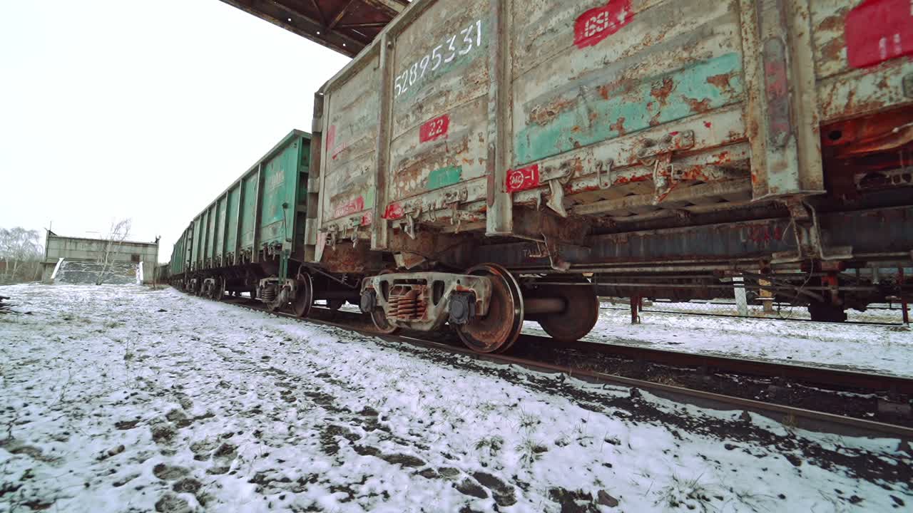 Row of multi-colored containers for cargo rides along the rails at the railway station and stops on the background of the ground covered with snow. View of bottom. Close-up.