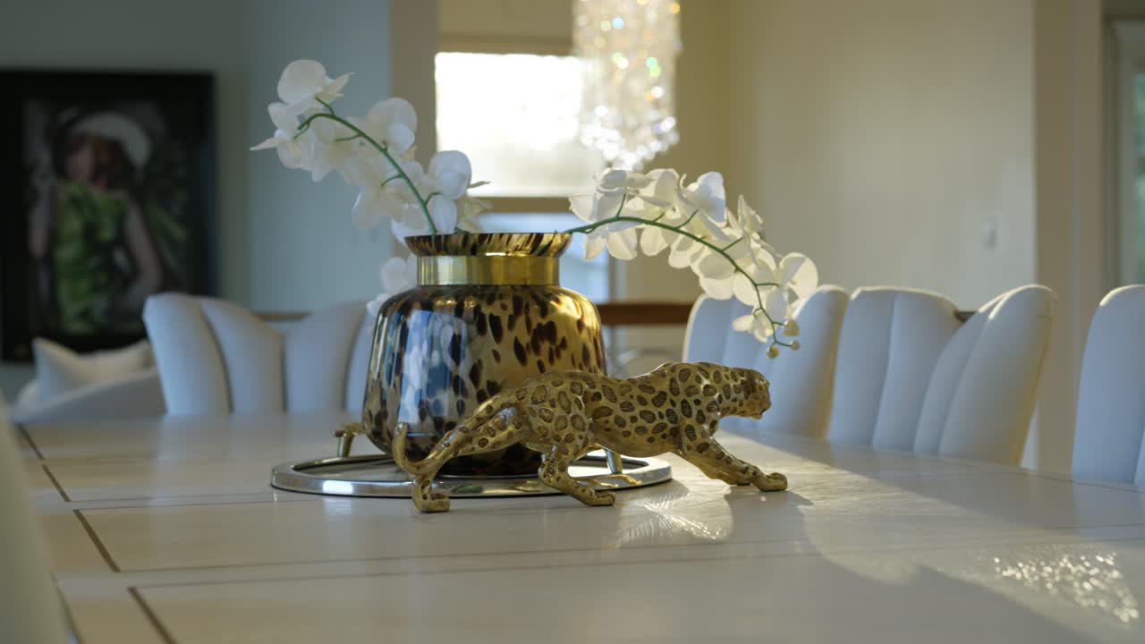 A cinematic shot of a golden jaguar figurine and golden vase with white flowers on top of a luxury white dinner table