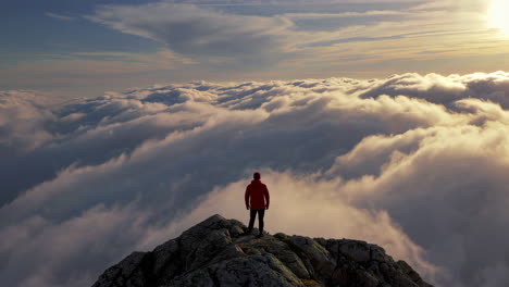 man standing on mountain peak above clouds at sunset