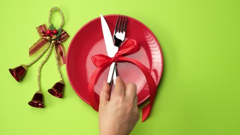 wo female hands put on a red round ceramic plate forks with a knife, top view