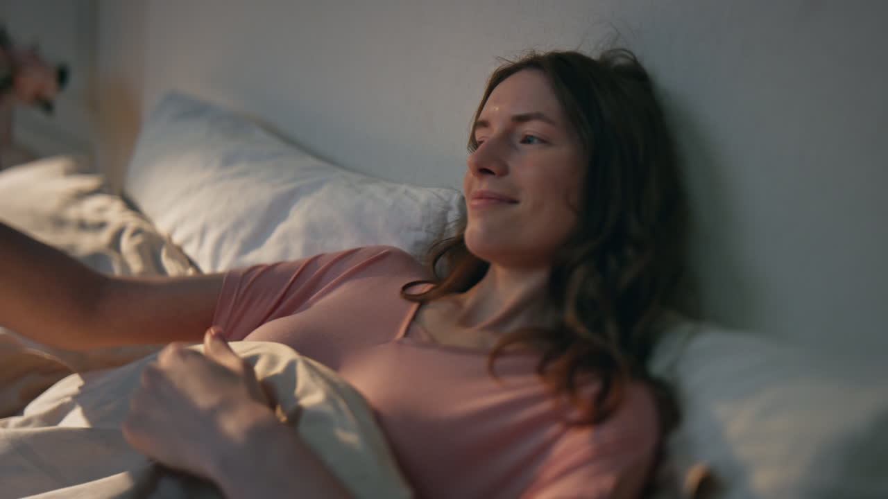 침대에서 아침을 즐기는 클로즈업 소녀. 웃는 평온한 여성 부드러운 베개에 누워