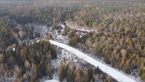 toma aérea de una carretera cubierta de nieve rodeada de un paisaje de bosque boreal