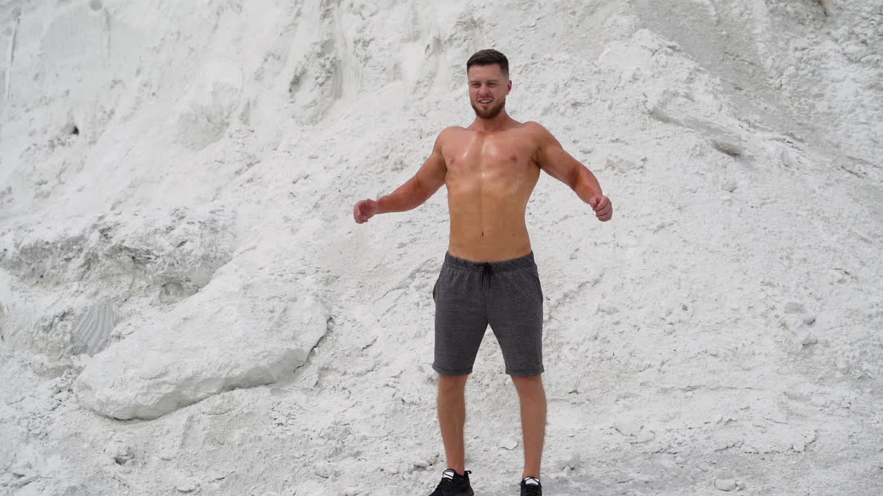Bearded man with muscular body poses on white mountain background. Strong bodybuilder outdoors in summer.