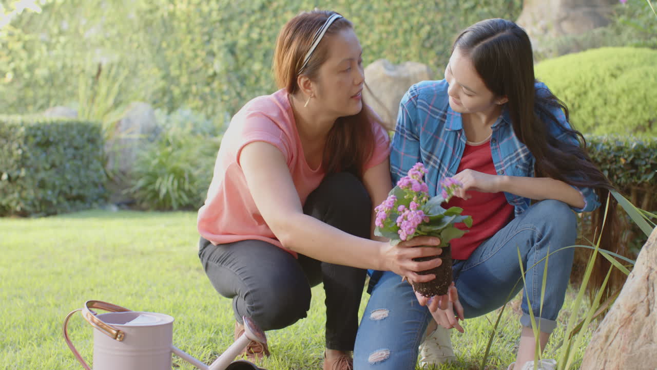 Planting flowers in garden, asian mother and daughter enjoying gardening together