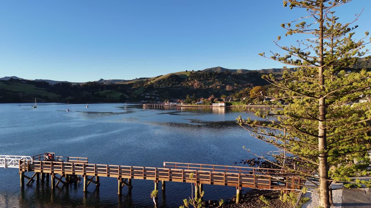 Aerial view of Akaroa's pier and calm waters at sunset, highlighting natural beauty and peaceful ambiance