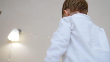 Mom's hand holding and shaking a pacifier above kid's head. Little boy gets a pacifier and puts it into mouth. Low angle view.