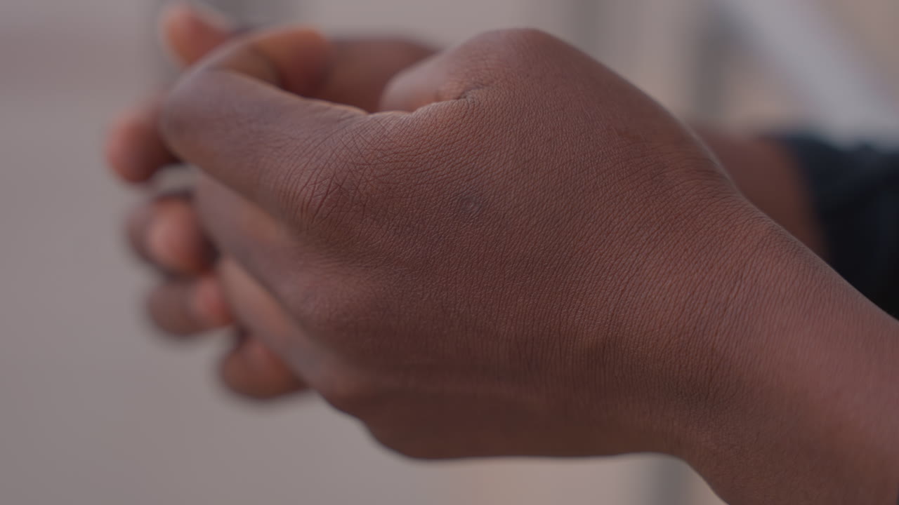 black hands closeup showing skin texture and fingertip movement, interlaced fingers, subtle callus and knuckle detail, careful rubbing and nervous gesture, muted background, emotionally tense study