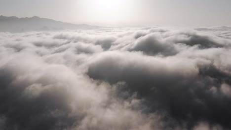 aerial view above thick clouds rolling over mountain peaks