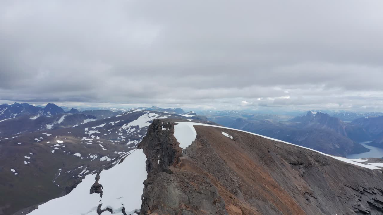fotografía de un dron de un pico dramático en el norte de noruega rodeado de nieve y montañas con un cielo dramático