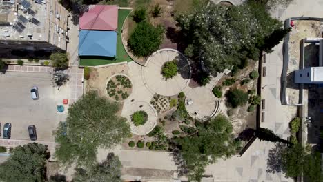zoom aéreo lento y tranquilo en toma de drones de un parque de barrio con suelo circular de hormigón, rodeado de edificios, árboles y arbustos