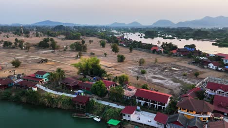 drone captures rice paddies and village homes in don det, laos, bordered by the mekong river and backed by the distant annamite mountains, as local farming and land preparation unfold at dusk