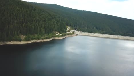 Drone-shot,-sideways-movement-over-a-lake-next-to-a-dam-on-a-cloudy-day-with-a-forest-in-the-background