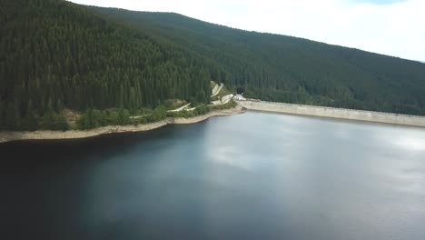 tir de drone, mouvement latéral au-dessus d'un lac à côté d'un barrage par temps nuageux avec une forêt en arrière-plan