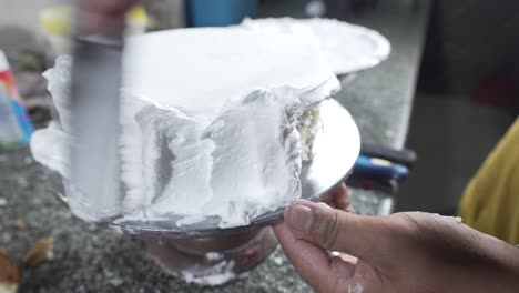 close up of hands smearing butter cream on chocolate cake by white spatula