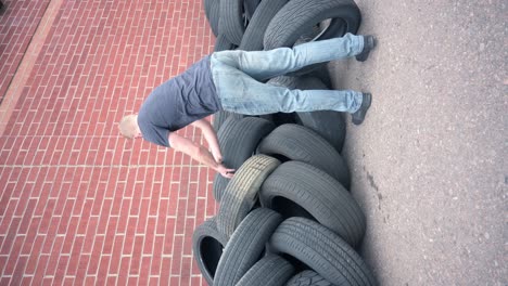 caucasian male stacking old used tires in front of a brick wall to be recycled, vertical