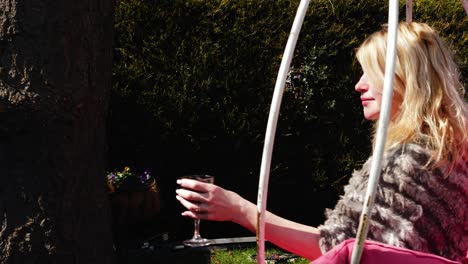 attractive woman enjoys glass of wine in garden chair swing wide 4k slow motion