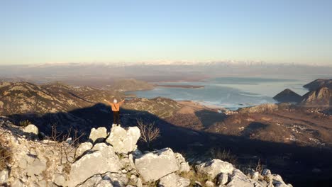 aéreo - persona que camina levanta los brazos en las montañas, lago skadar, montenegro, marcha atrás