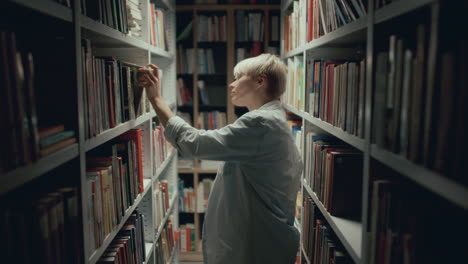 woman walking among bookshelves, looking for book in library