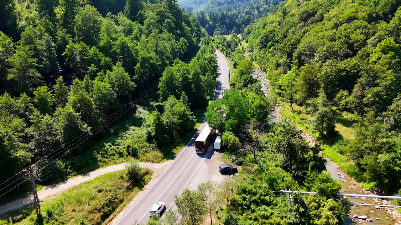 Trucks driving through green mountain pass. Freight vehicles move along a mountain road beside a rocky shallow stream
