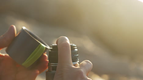 man-opens-thermos-as-steam-of-hot-drink-evaporate-he-pours-coffee-in-cup-and-takes-a-sip-during-golden-hour