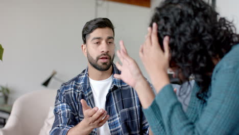 una pareja biracial sentada en el sofá y discutiendo en casa, en cámara lenta.