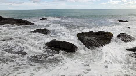 Aerial-dolly-in-of-foamy-waves-hitting-the-rocky-shore-and-turquoise-sea-in-Dominicalito-Beach,-Costa-Rica