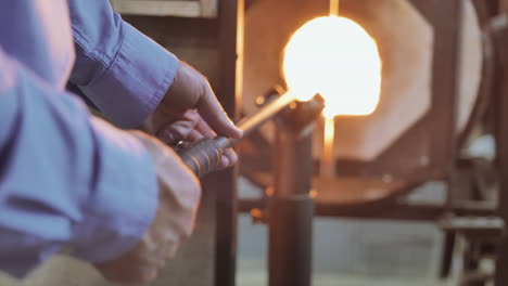 glass artist rotates rod inserted into white hot furance, melting glass