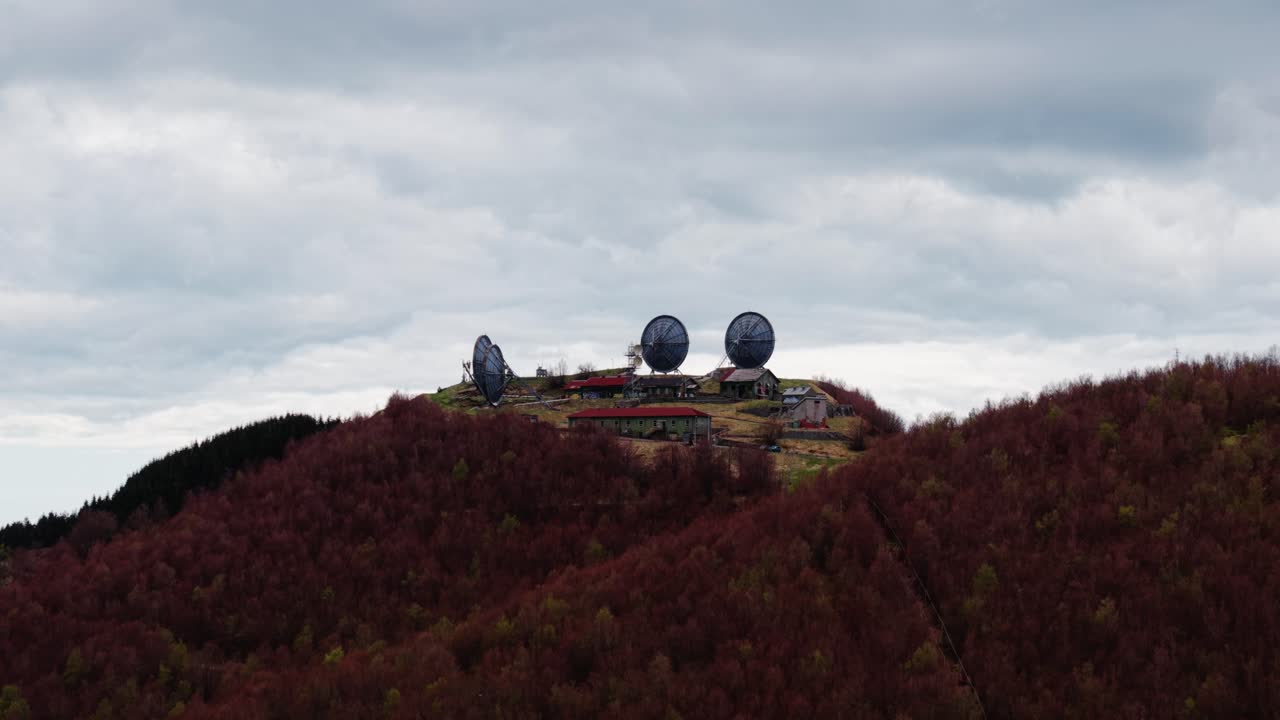 Old radar station on a forested mountain, aerial shot under cloudy skies