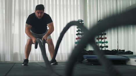 hombre que usa cuerdas de batalla para hacer ejercicio en un gimnasio